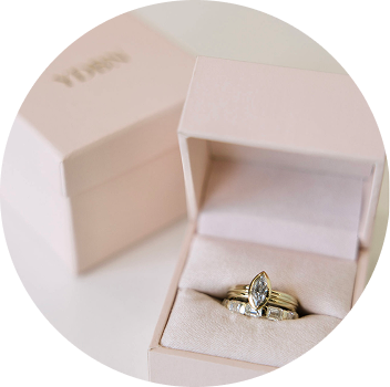 A gold engagement ring and wedding bands displayed in a pink jewelry box.