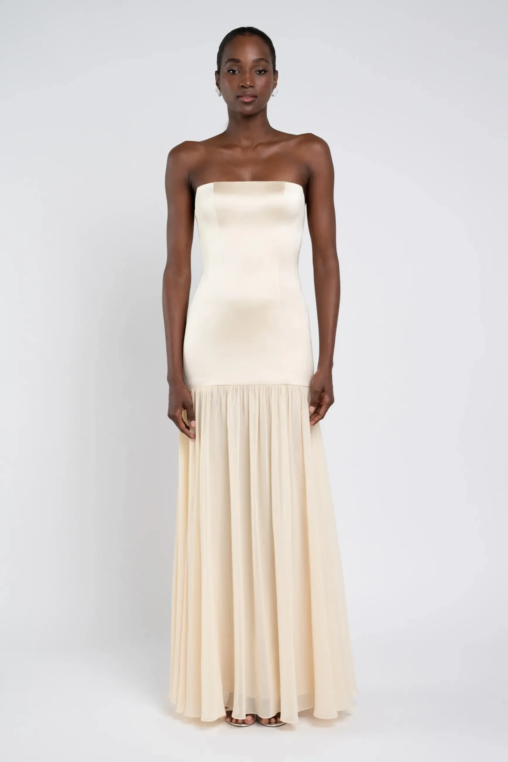 A model wearing a strapless, cream-colored evening gown that flows elegantly to the floor.