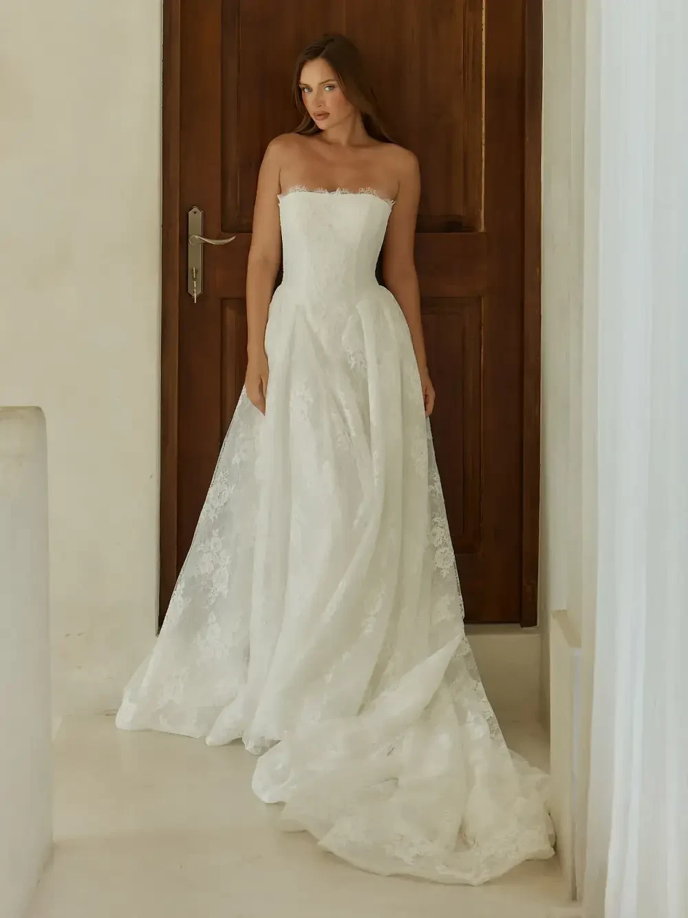 A woman in a strapless white wedding dress standing in front of a wooden door.